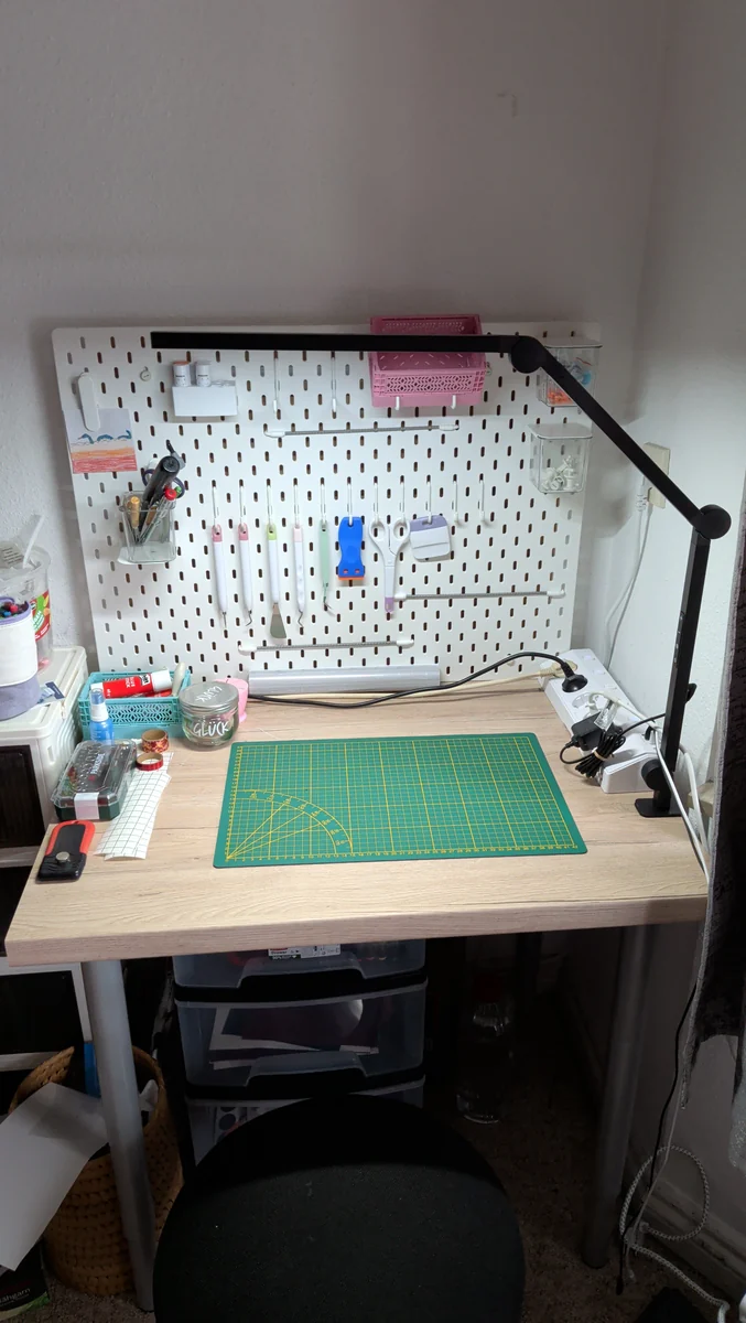 Arbeitsplatz mit Lochwand voller Plotterwerkzeuge, Schneidematte und Lampe